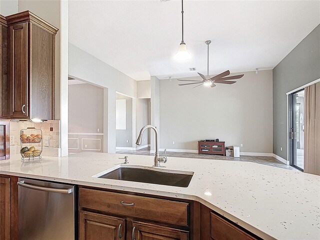 kitchen with stainless steel dishwasher, a ceiling fan, light stone countertops, a sink, and decorative light fixtures