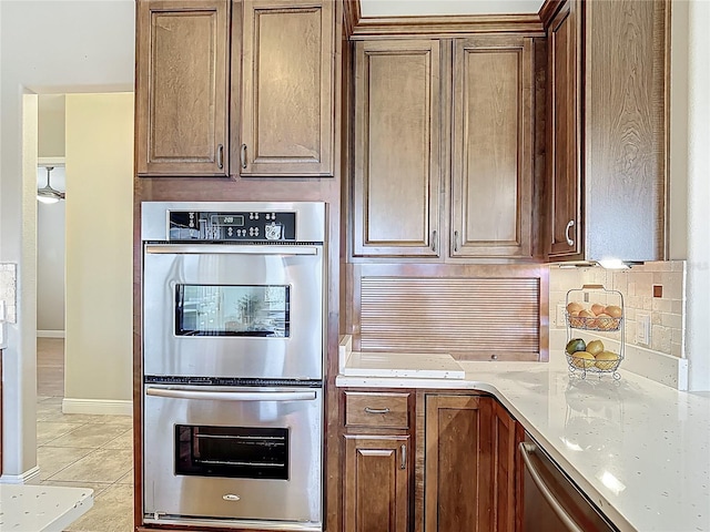 kitchen with light tile patterned floors, decorative backsplash, light stone countertops, and stainless steel appliances