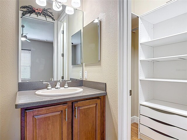 bathroom with vanity, a textured wall, ceiling fan, and wood finished floors