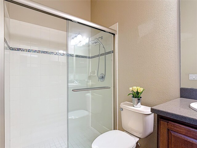 full bathroom with toilet, a textured wall, a shower stall, and vanity