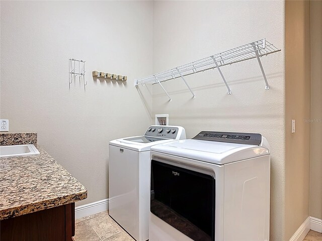 clothes washing area featuring washer and dryer, laundry area, baseboards, and a sink