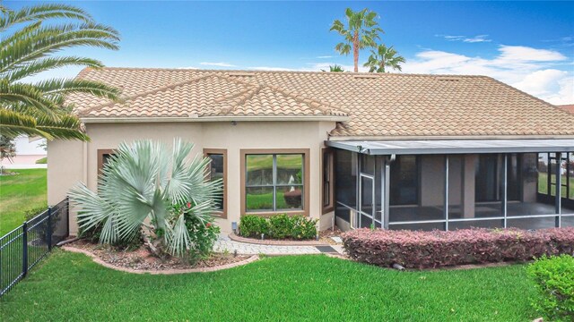rear view of property featuring fence, a tile roof, stucco siding, a sunroom, and a lawn