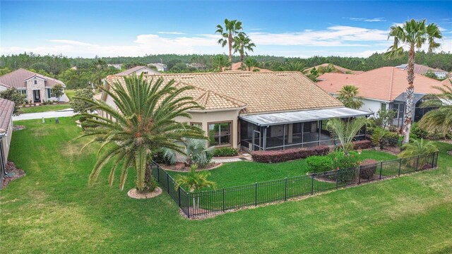 back of property featuring a fenced backyard, a yard, a sunroom, and a tile roof