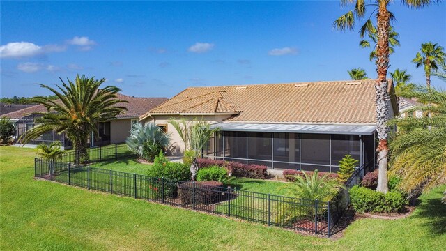 rear view of house featuring stucco siding, a sunroom, a fenced backyard, a tiled roof, and a yard