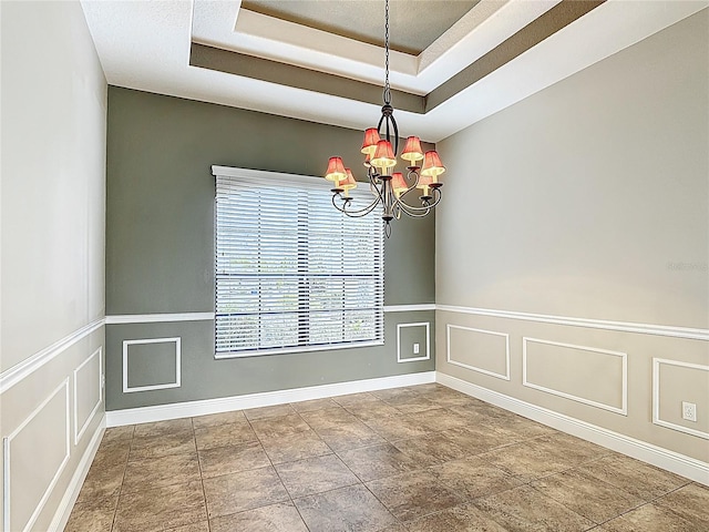 empty room with baseboards, a notable chandelier, a raised ceiling, and a wainscoted wall