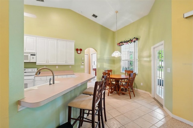 2374 Eagle Trace Dr, Kissimmee, FL 34746 - kitchen with white appliances, a breakfast bar area, white cabinets, visible vents, and high vaulted ceiling