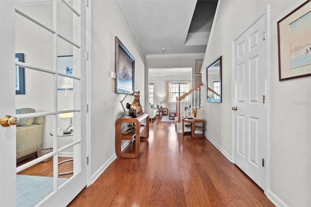 corridor featuring baseboards, ornamental molding, stairs, and wood finished floors