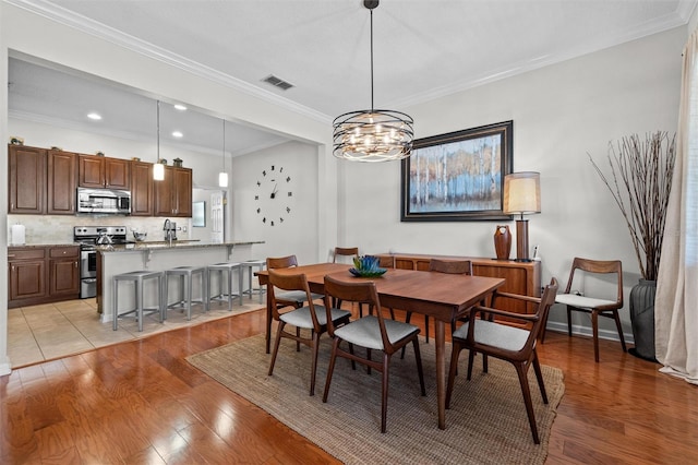 dining area featuring visible vents, a notable chandelier, light wood-style floors, and crown molding