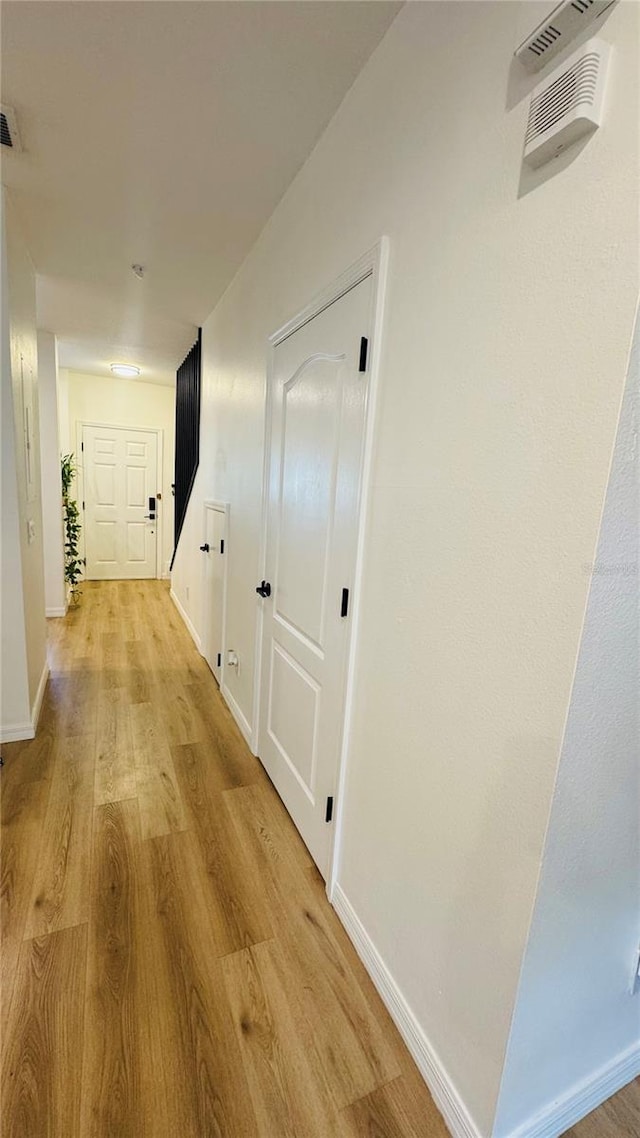 hall featuring light wood-type flooring, baseboards, and visible vents