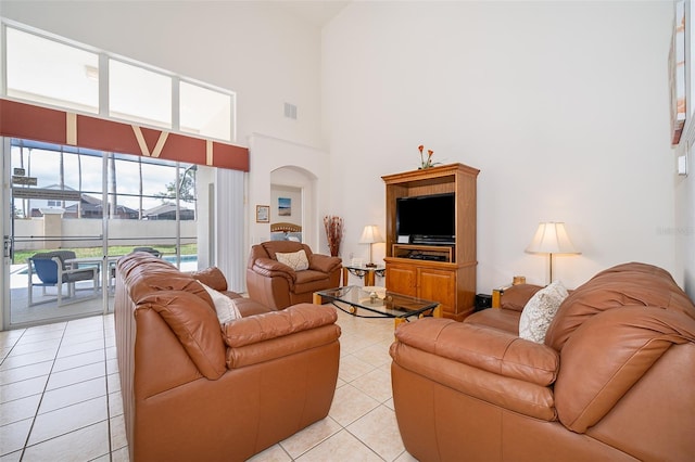 living area featuring arched walkways, visible vents, light tile patterned flooring, and a towering ceiling