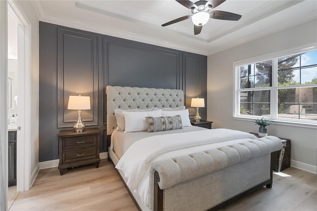 bedroom with a tray ceiling, light wood-type flooring, a ceiling fan, baseboards, and ornamental molding