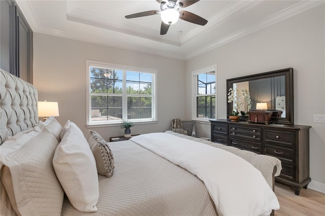 bedroom featuring baseboards, light wood-type flooring, a ceiling fan, crown molding, and a tray ceiling