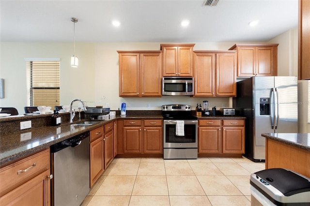 kitchen featuring a sink, stainless steel appliances, dark stone countertops, brown cabinetry, and decorative light fixtures