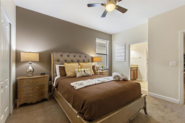 bedroom featuring light colored carpet, ensuite bathroom, a ceiling fan, and baseboards