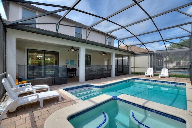 view of pool featuring glass enclosure, a patio area, ceiling fan, and a pool with connected hot tub