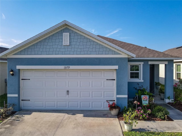 view of front facade featuring concrete driveway, a garage, stucco siding, and roof with shingles