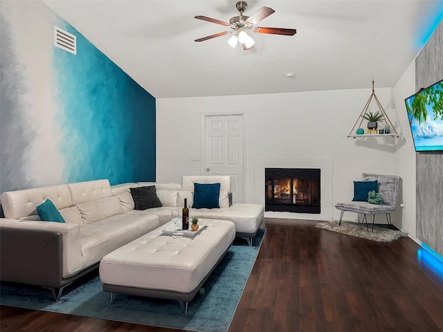 living area with a lit fireplace, a ceiling fan, visible vents, vaulted ceiling, and wood finished floors