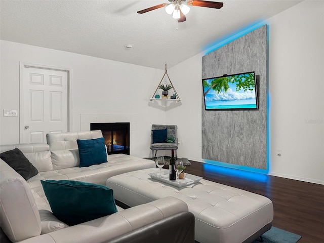 living area with a glass covered fireplace, wood finished floors, lofted ceiling, baseboards, and ceiling fan