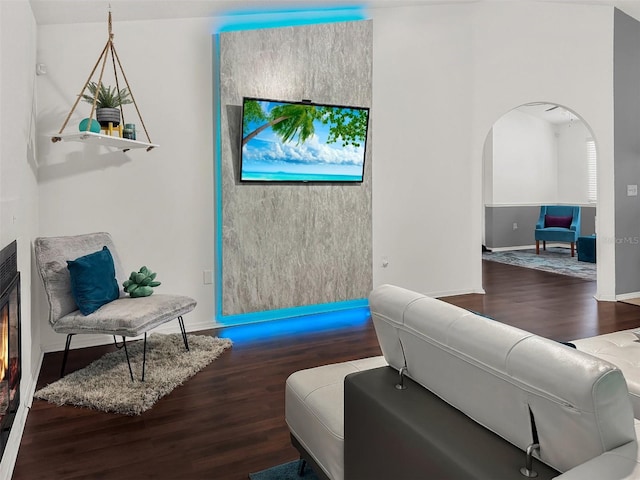 living room with baseboards, arched walkways, wood finished floors, and a warm lit fireplace