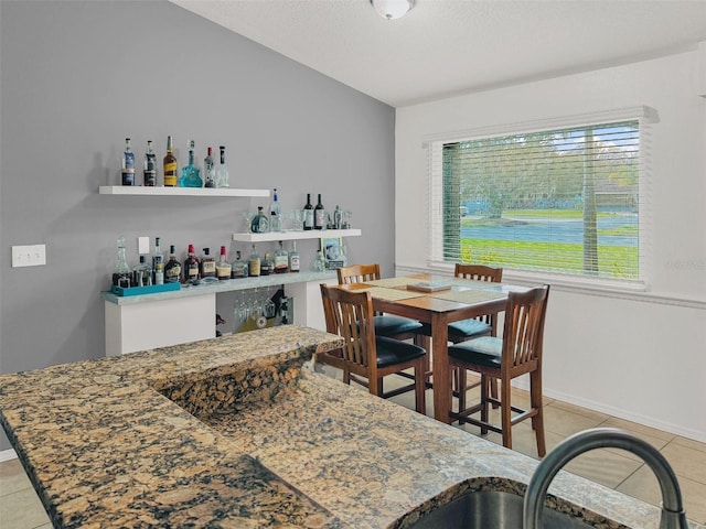 dining space with baseboards, light tile patterned floors, and indoor bar