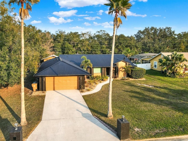 ranch-style home featuring an attached garage, driveway, metal roof, and a front yard