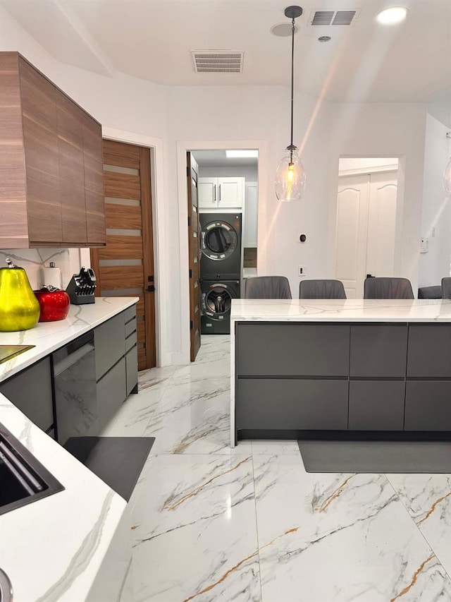 kitchen featuring pendant lighting, stacked washer and clothes dryer, modern cabinets, and visible vents