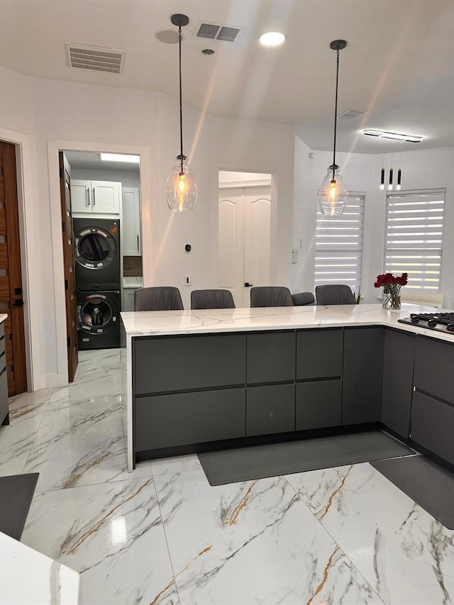 kitchen featuring stacked washer and clothes dryer, gray cabinetry, visible vents, stainless steel gas cooktop, and hanging light fixtures