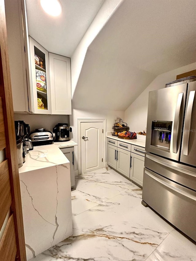 kitchen featuring light stone countertops, glass insert cabinets, stainless steel fridge with ice dispenser, vaulted ceiling, and marble finish floor