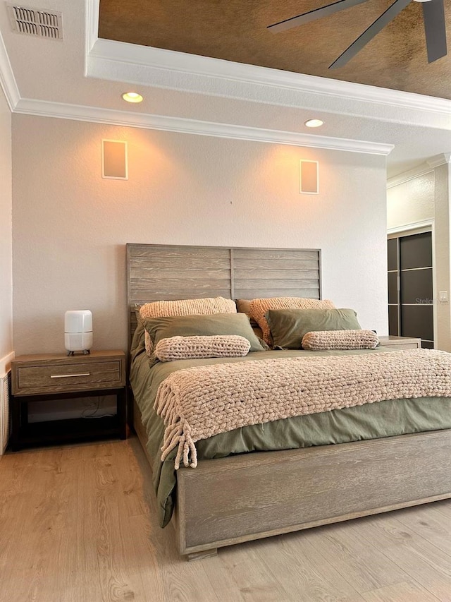 bedroom with visible vents, wood finished floors, crown molding, and a tray ceiling