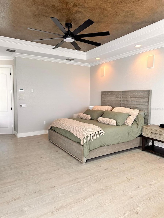 bedroom with visible vents, wood finished floors, crown molding, and a tray ceiling