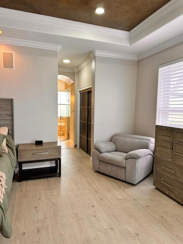 bedroom with crown molding, arched walkways, a raised ceiling, and light wood-type flooring