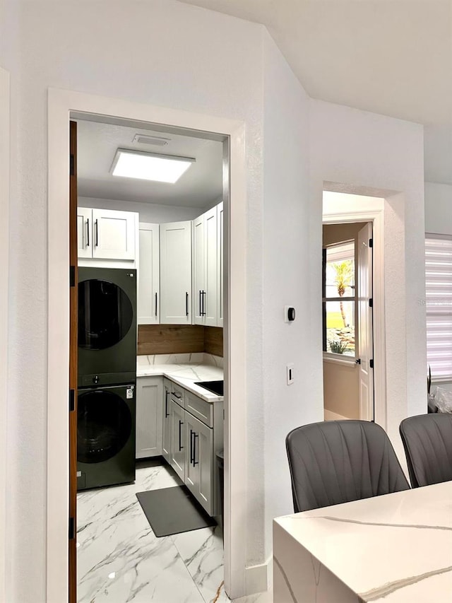 kitchen featuring stacked washer and dryer, light countertops, and marble finish floor