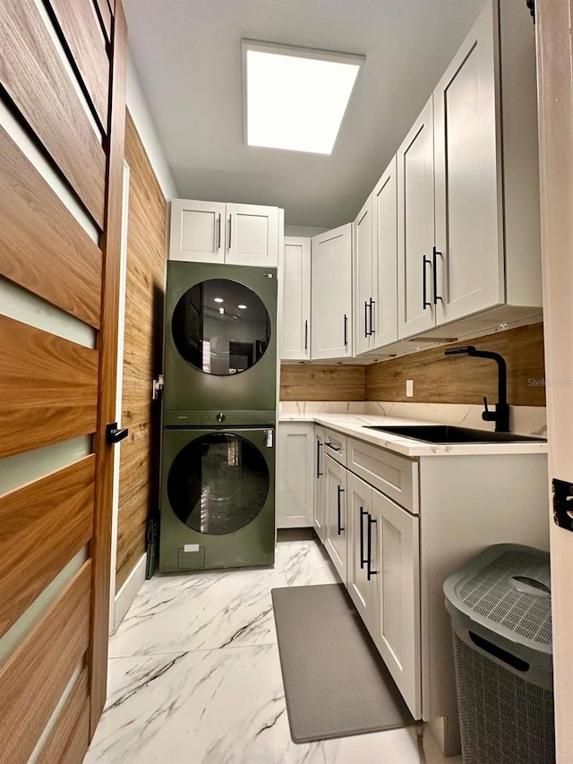 laundry area with stacked washer / drying machine, cabinet space, marble finish floor, and a sink