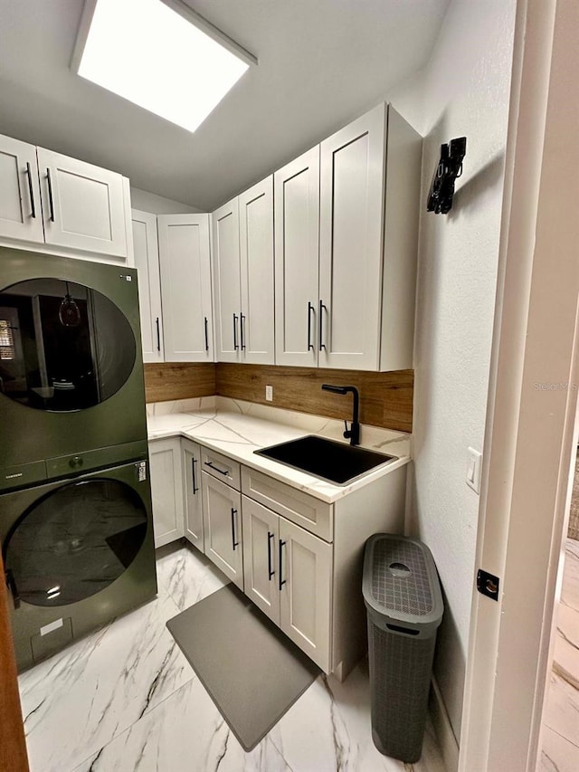 laundry room with stacked washer and dryer, cabinet space, marble finish floor, and a sink