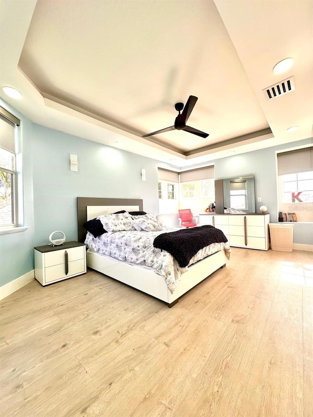 bedroom with multiple windows, wood finished floors, a raised ceiling, and visible vents