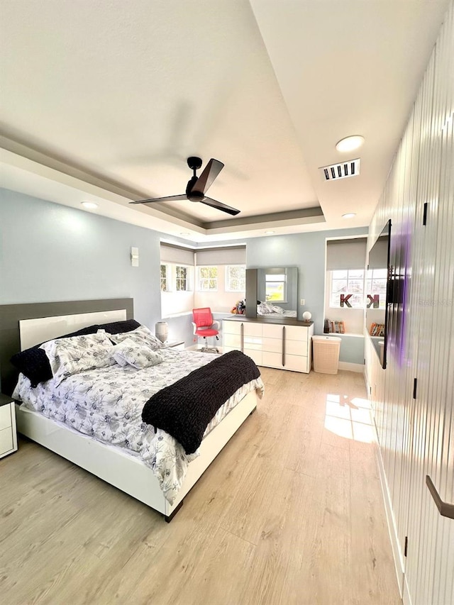 bedroom featuring visible vents, light wood-style flooring, and a tray ceiling