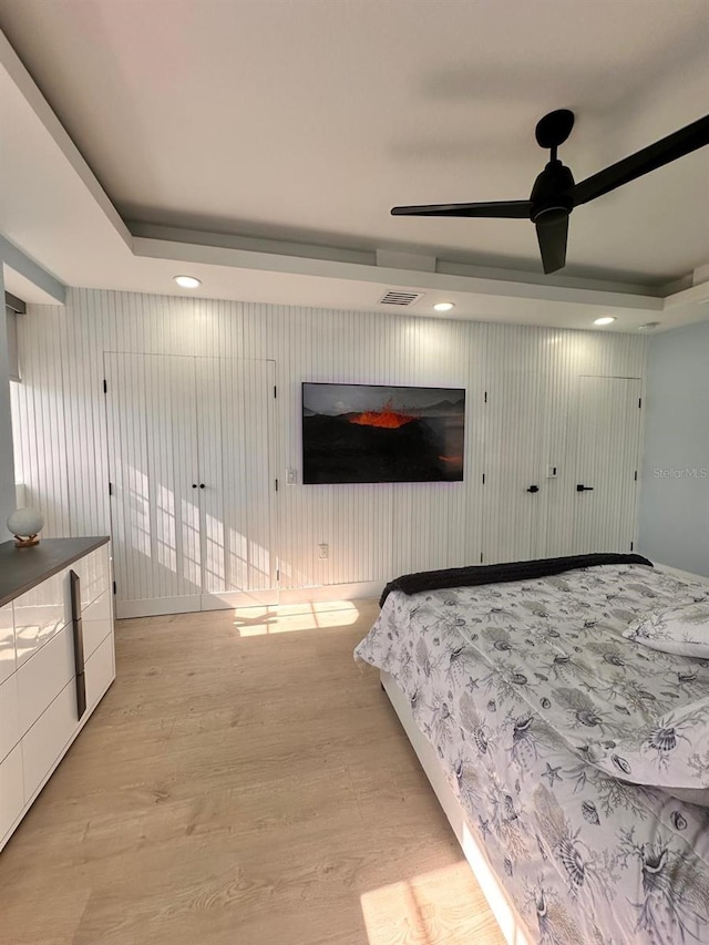 bedroom featuring recessed lighting, visible vents, light wood-style flooring, and a tray ceiling