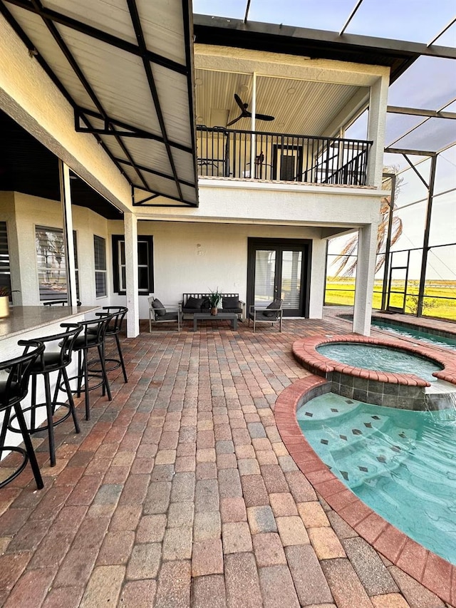 view of patio with a lanai, ceiling fan, a balcony, and a pool with connected hot tub