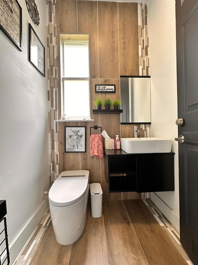 half bathroom with wood finished floors, toilet, and vanity