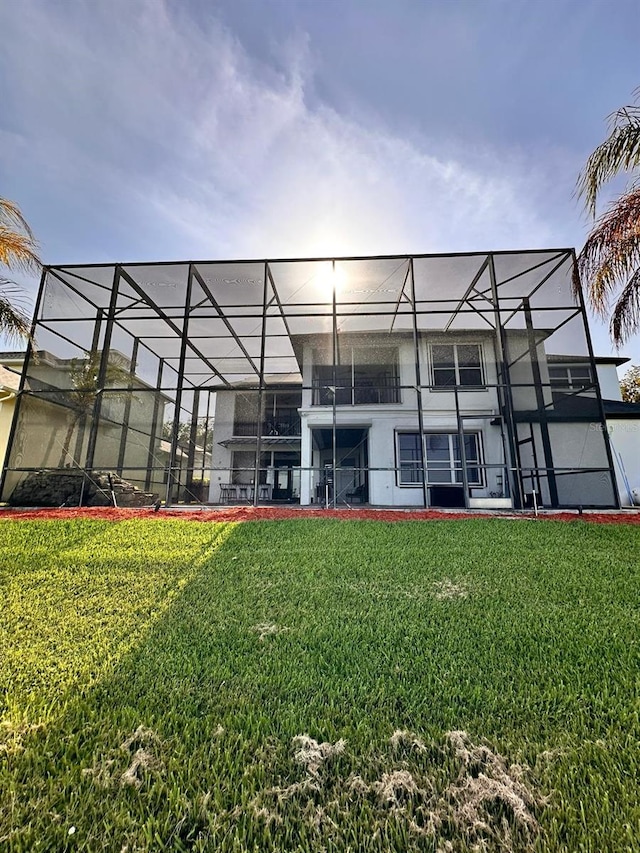 rear view of property with a lawn, stucco siding, and glass enclosure