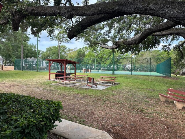 view of home's community featuring a tennis court, a yard, and fence