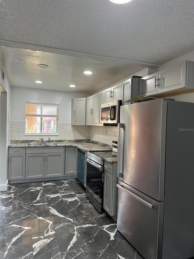 kitchen with tasteful backsplash, recessed lighting, appliances with stainless steel finishes, a sink, and gray cabinetry
