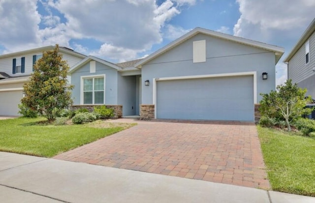 ranch-style house featuring stone siding, a garage, stucco siding, a front yard, and decorative driveway