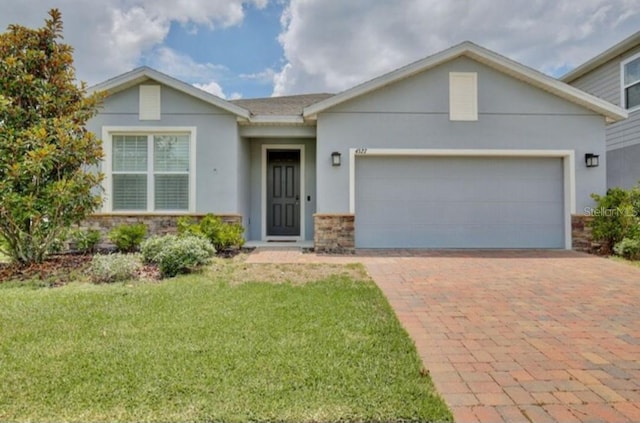 ranch-style home with a garage, decorative driveway, a front lawn, stone siding, and stucco siding