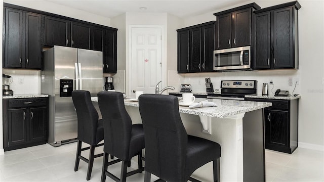 kitchen featuring a breakfast bar area, stainless steel appliances, backsplash, and dark cabinetry