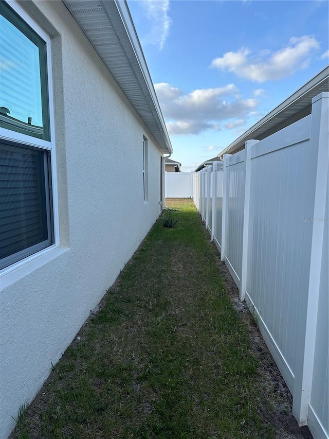 view of property exterior with stucco siding, a lawn, and a fenced backyard