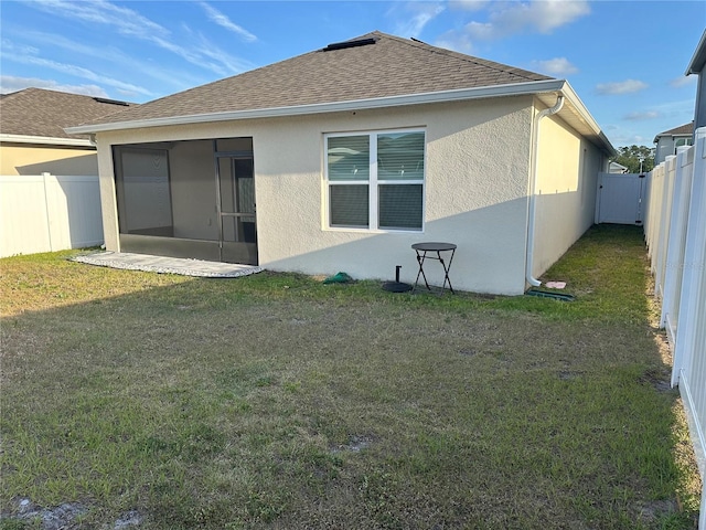 back of property with a fenced backyard, stucco siding, a shingled roof, a sunroom, and a lawn