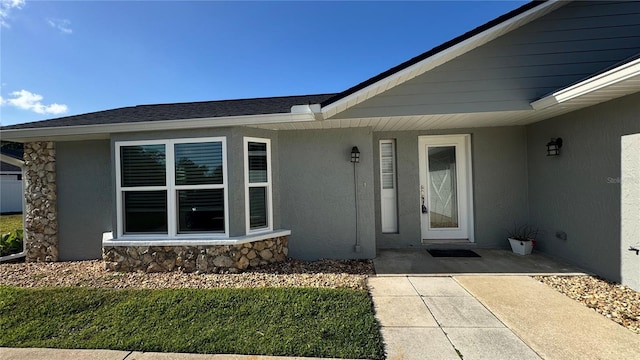 property entrance with roof with shingles, stucco siding, and stone siding