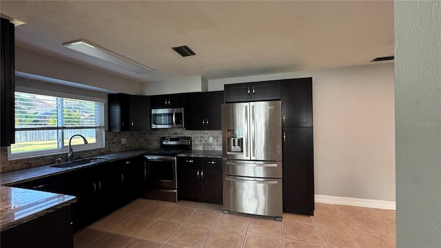 kitchen with a sink, stainless steel appliances, visible vents, decorative backsplash, and dark cabinetry