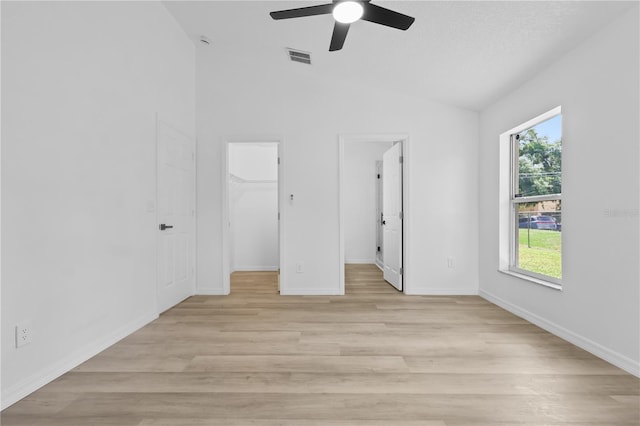 unfurnished bedroom featuring light wood-style floors, visible vents, a walk in closet, vaulted ceiling, and baseboards
